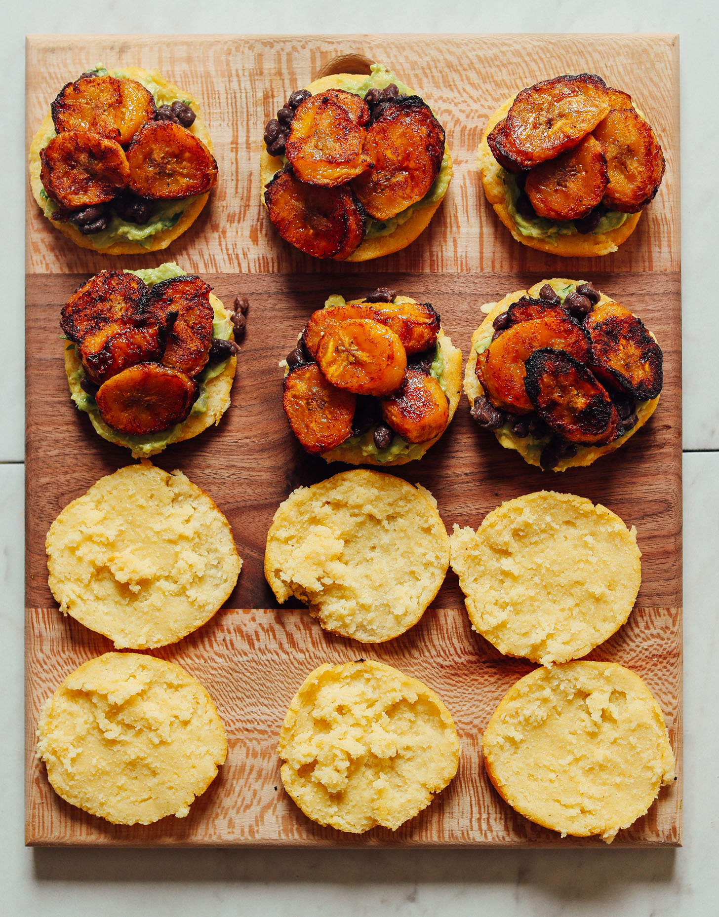 Open-faced Vegan Arepa Sandwiches topped with guacamole, black beans, and plantains