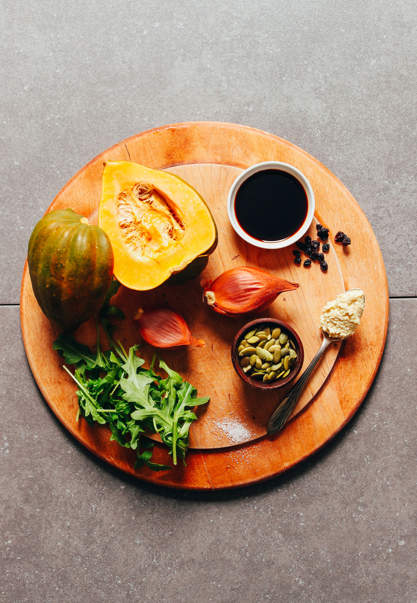 Wood cutting board with acorn squash, shallots and other ingredients for making a delicious plant-based fall salad