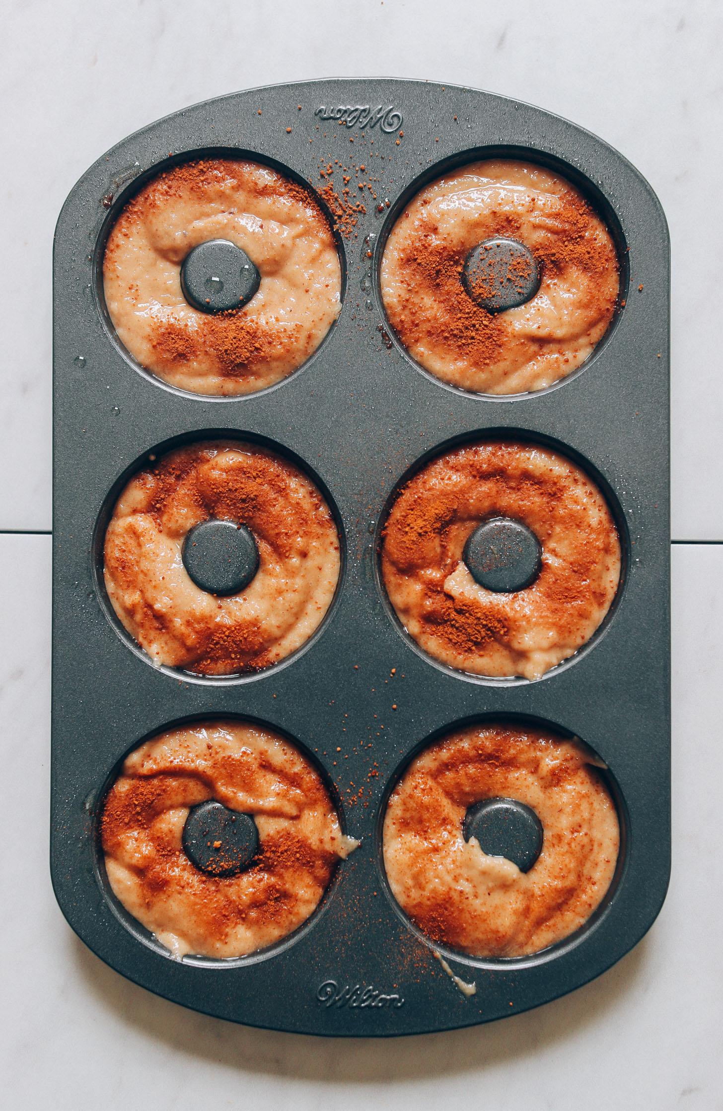 Vegan Gluten-Free Apple Cider donut batter sprinkled with cinnamon in a donut pan