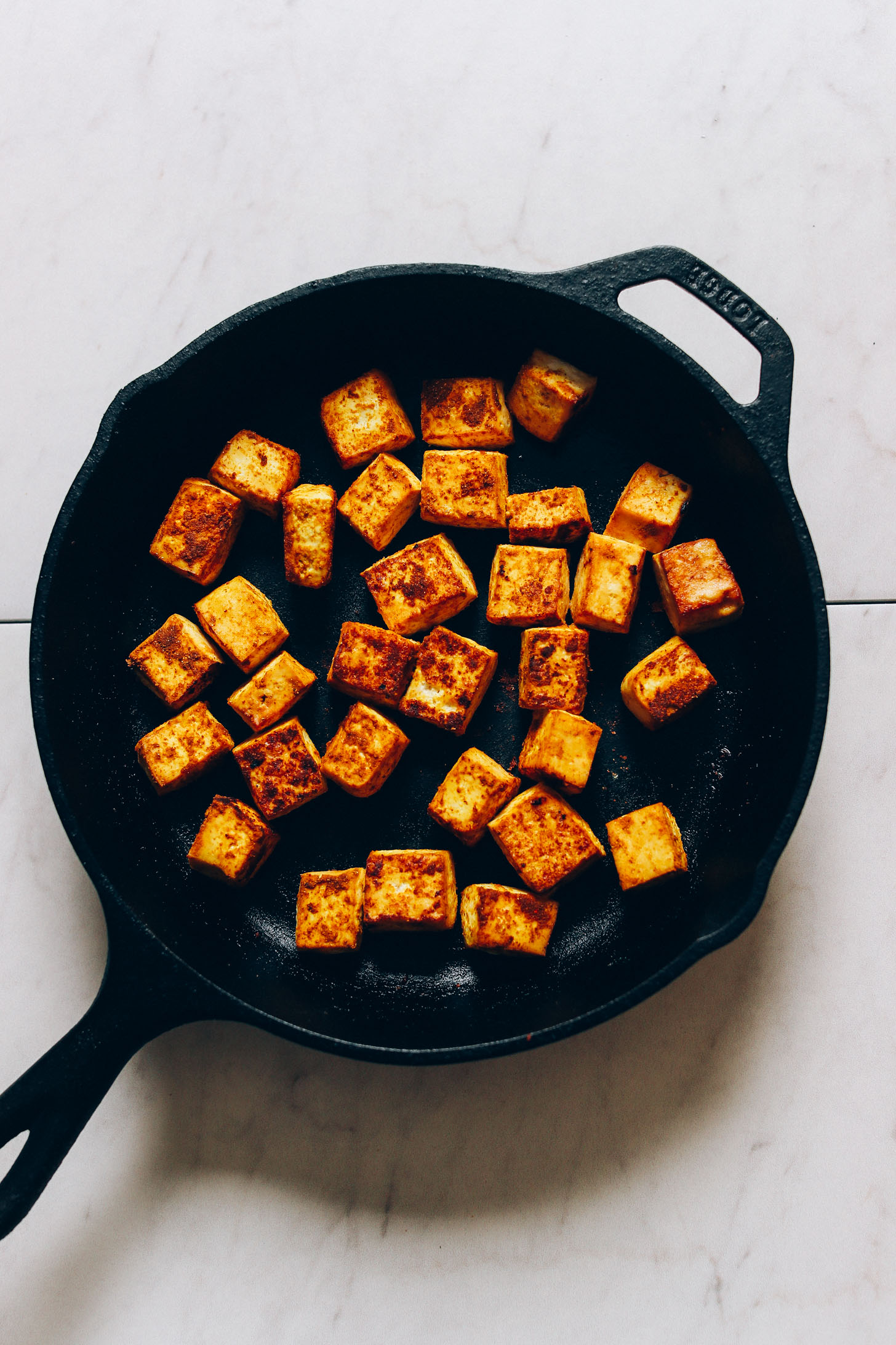 Overhead image of tofu being browned in a cast iron skillet with curry spices