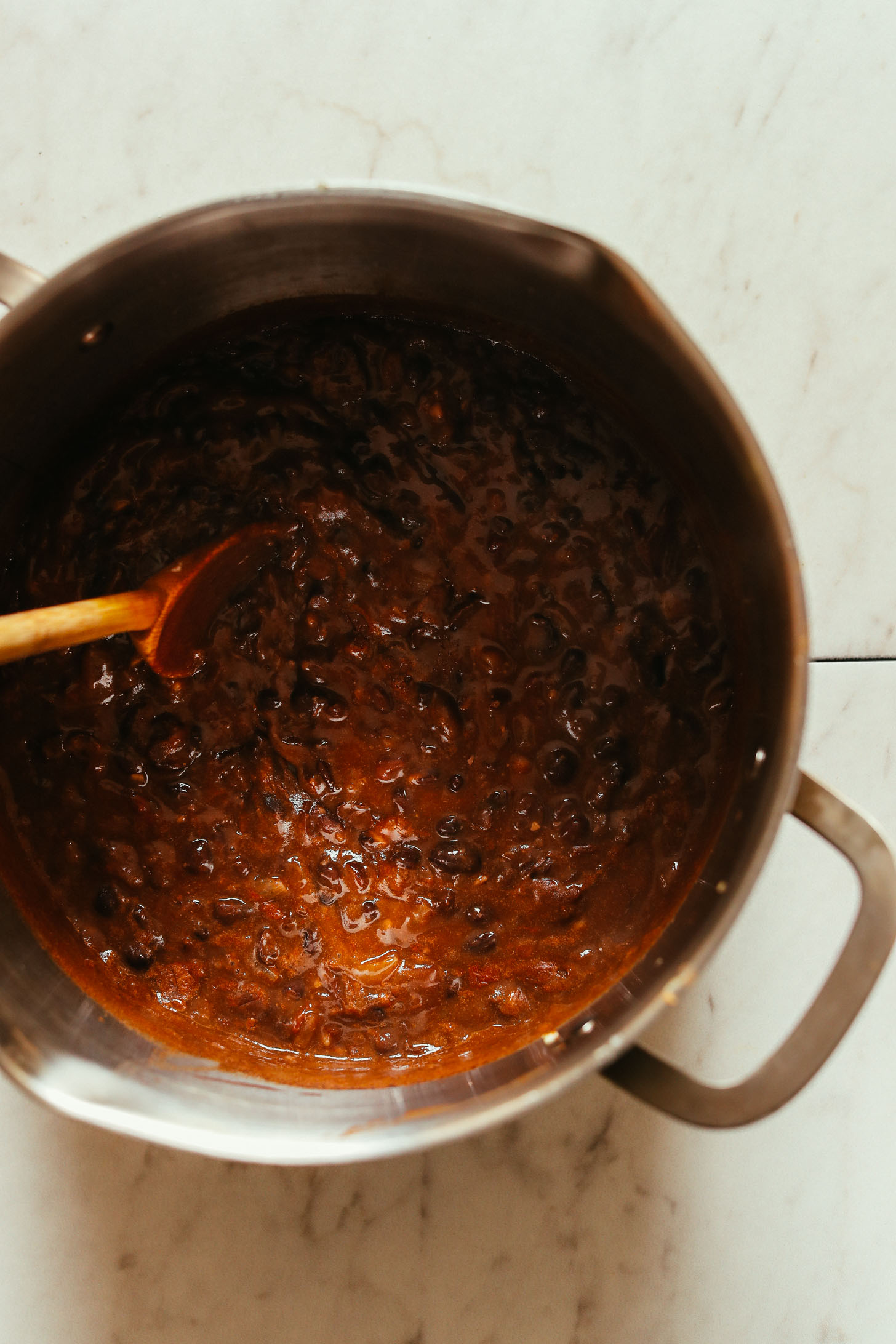 Overhead image of pot with black bean soup and a wooden spoon stirring the ingredients
