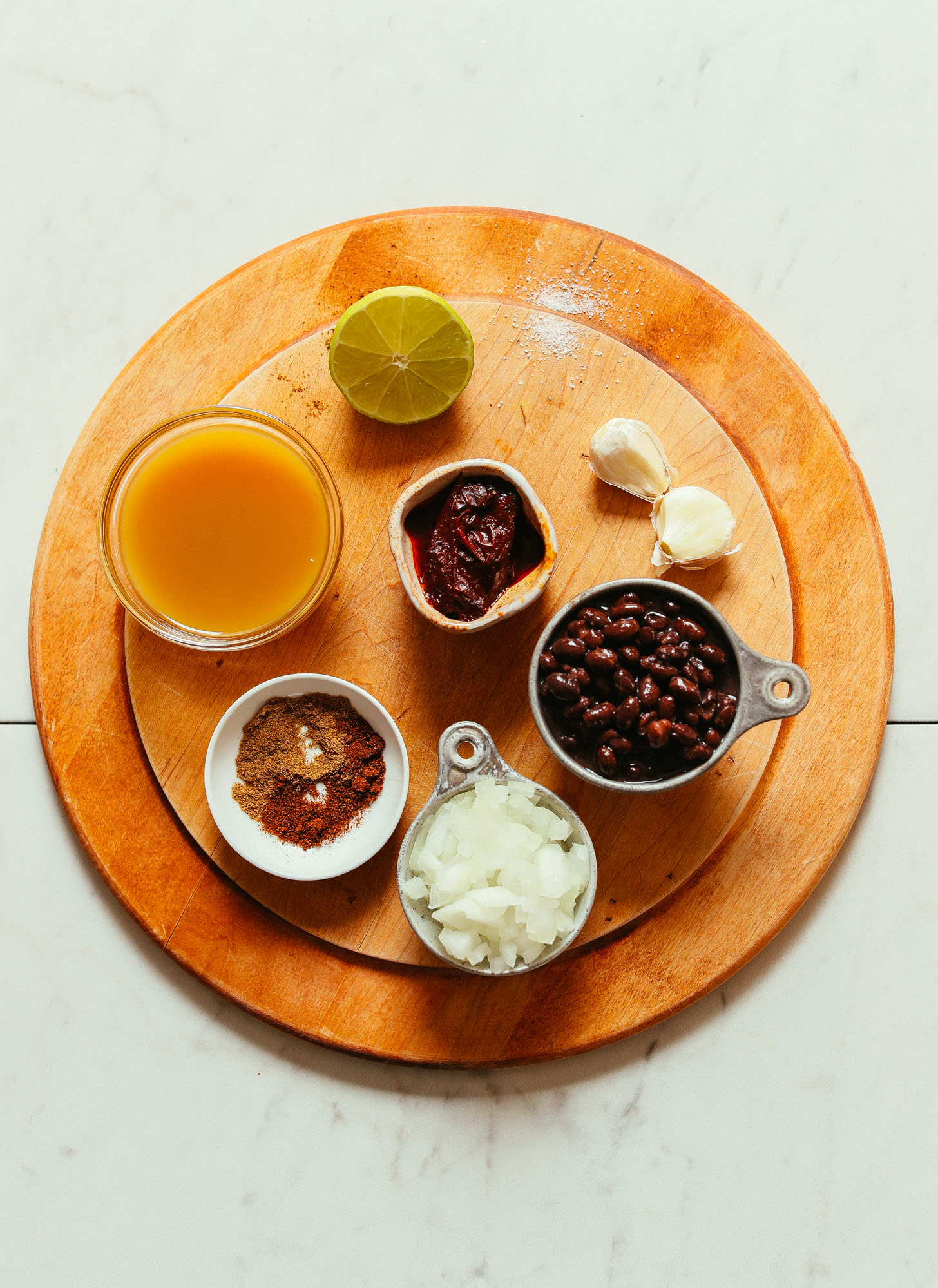 Overhead image of cutting board holding ingredients for black bean soup, including black beans, onion, lime, and vegetable broth