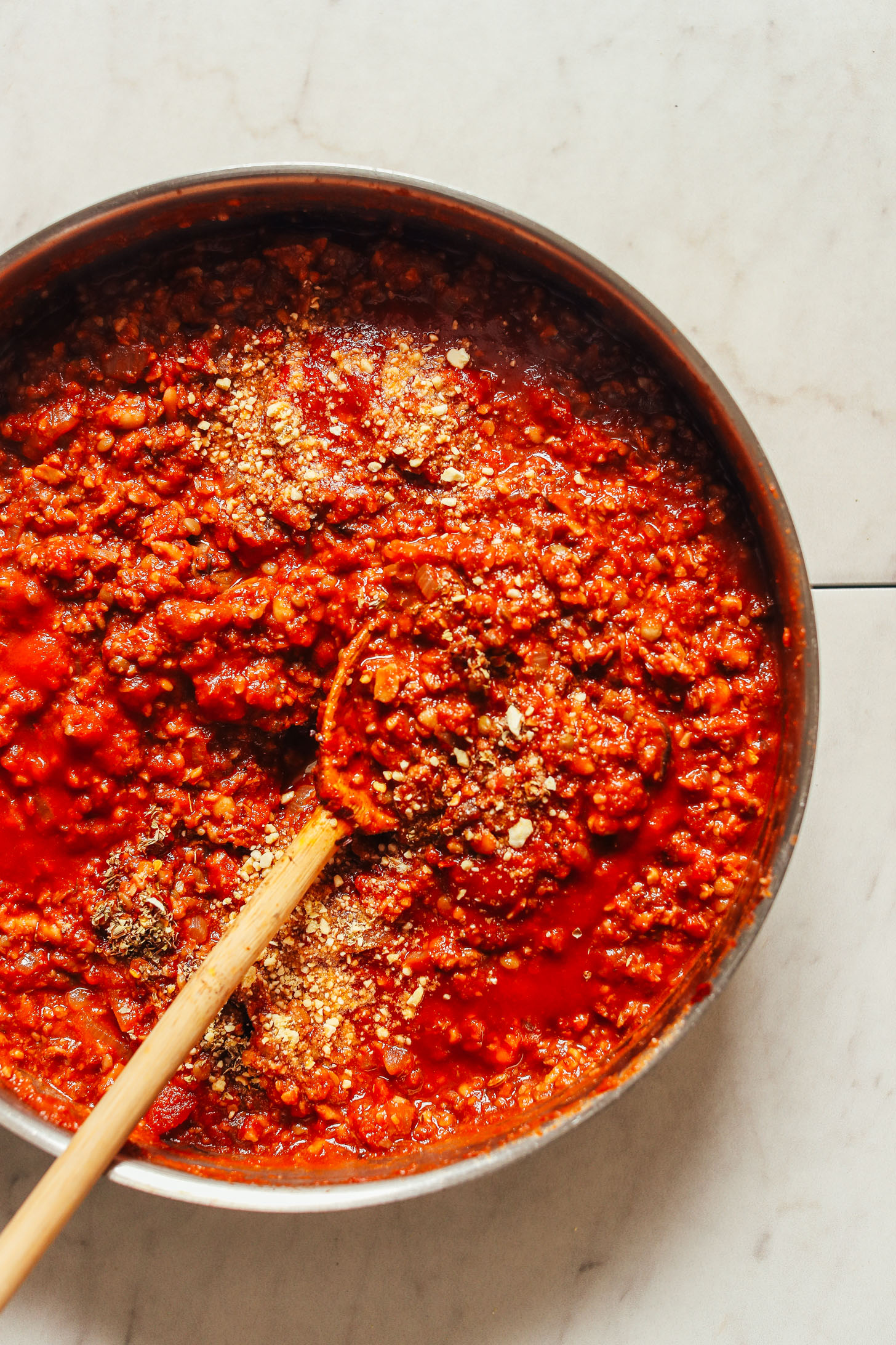 Overhead image of tempeh bolognese being stirred with a wooden spoon