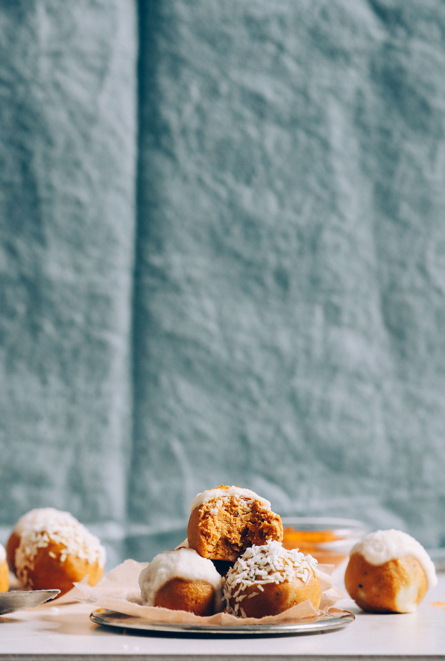 A straight on image of golden milk snack balls stacked in a small pile with coconut butter and coconut flakes as frosting and garnish