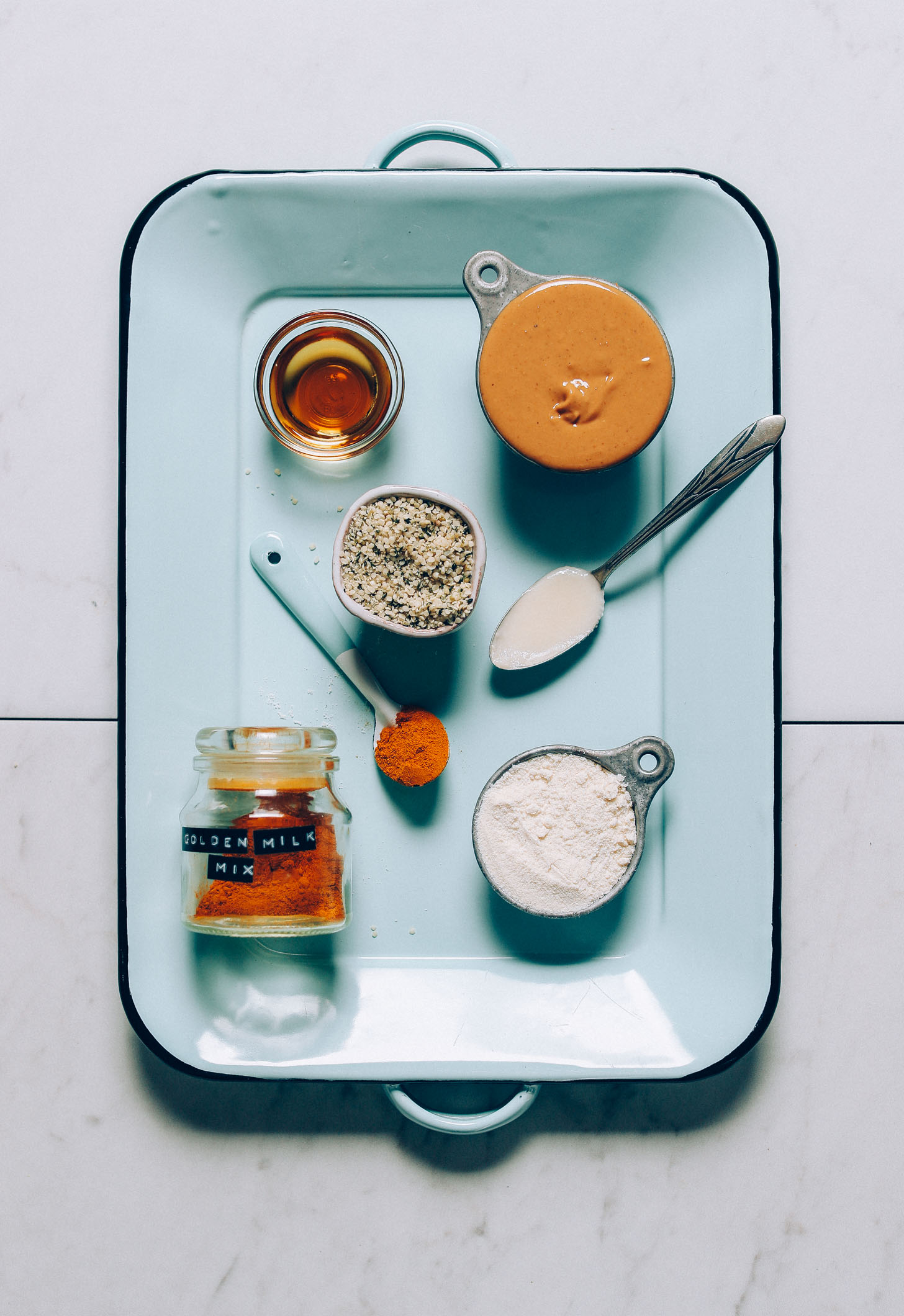An overhead image of ingredients for golden milk snack balls: maple syrup, hemp seeds, cashew butter, coconut flour, coconut butter, golden milk mix