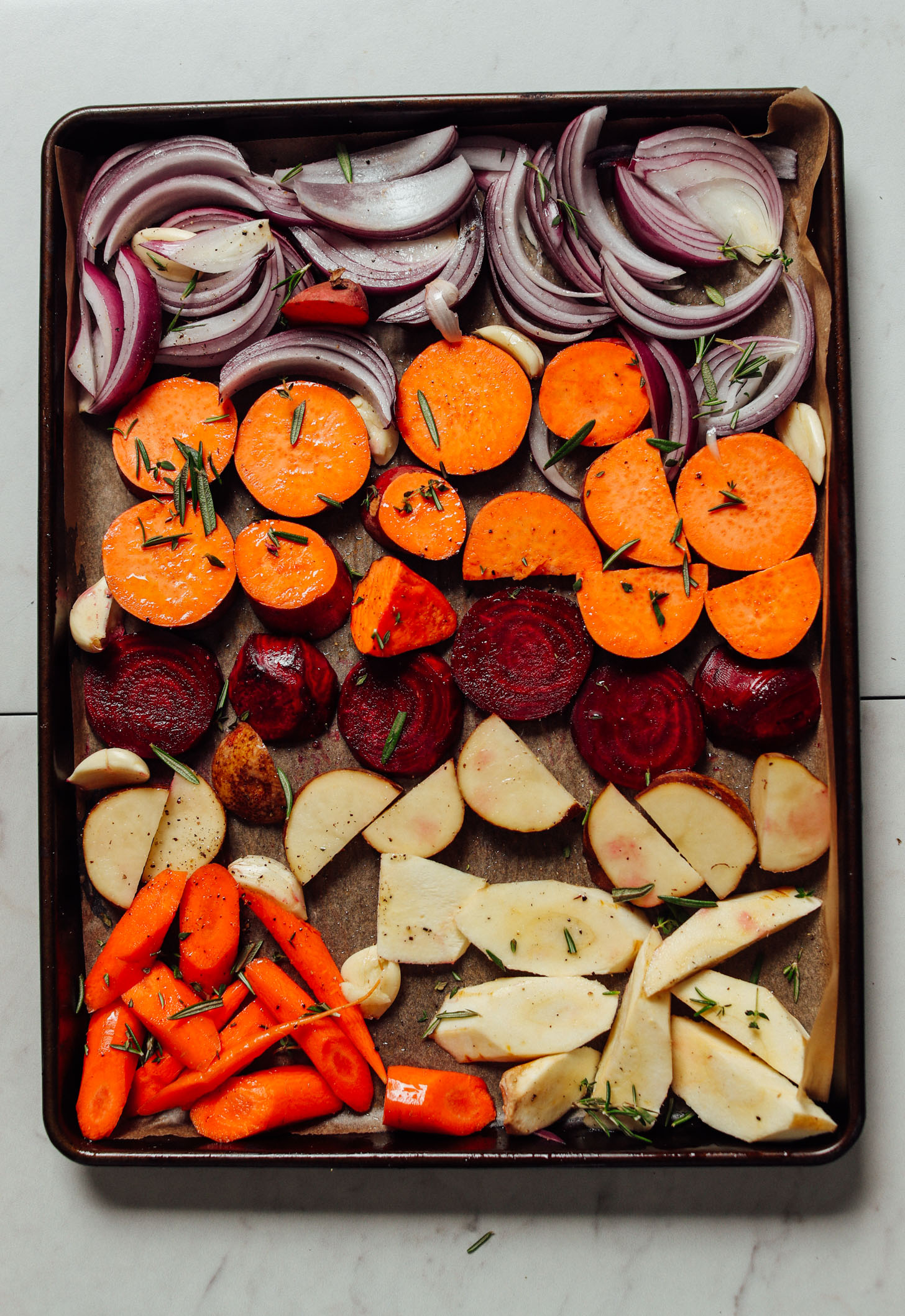 Parchment-lined baking sheet filled with sliced vegetables and herbs for roasting