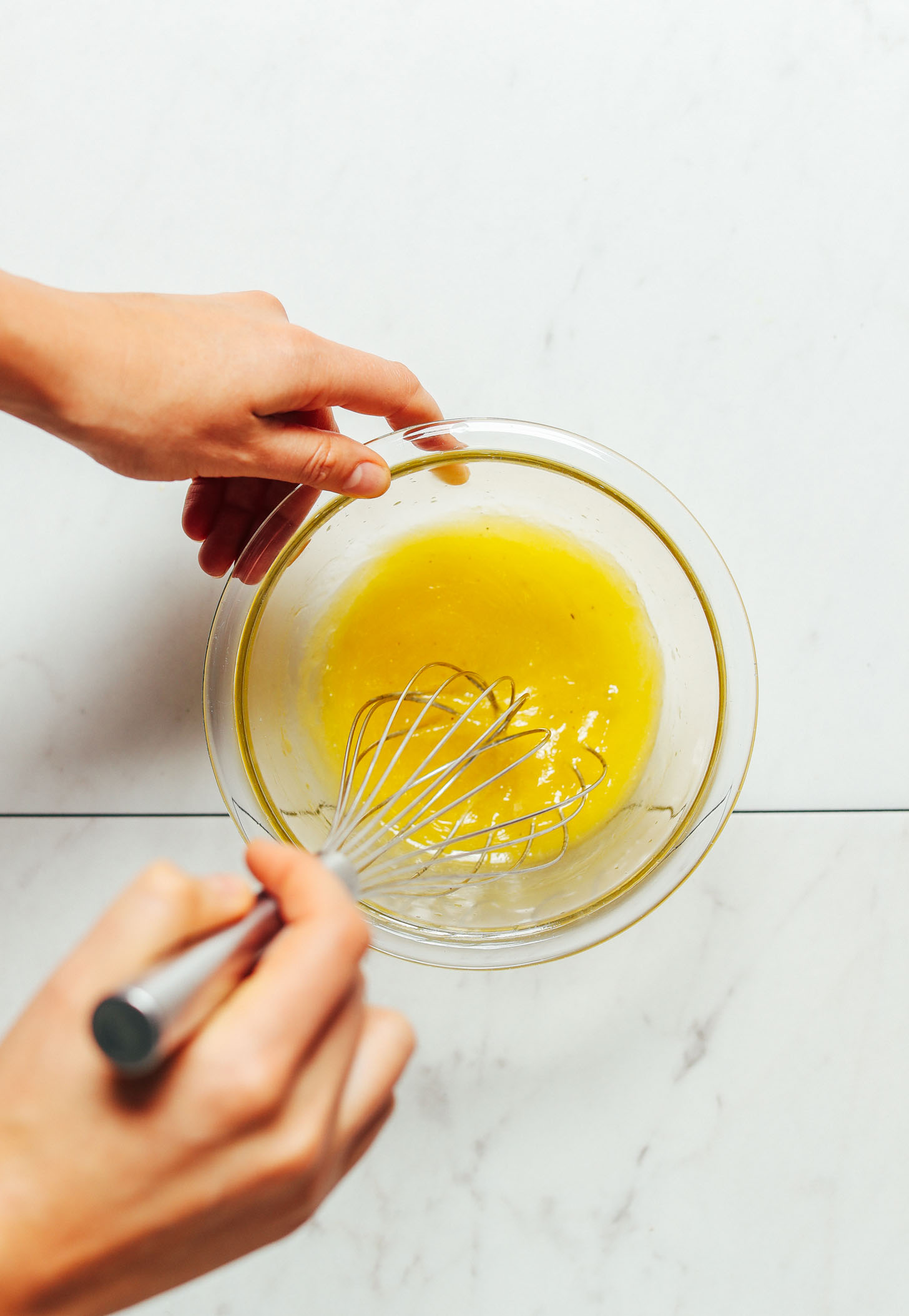 Overhead image of lemon vinaigrette in a glass bowl being whisked by hand
