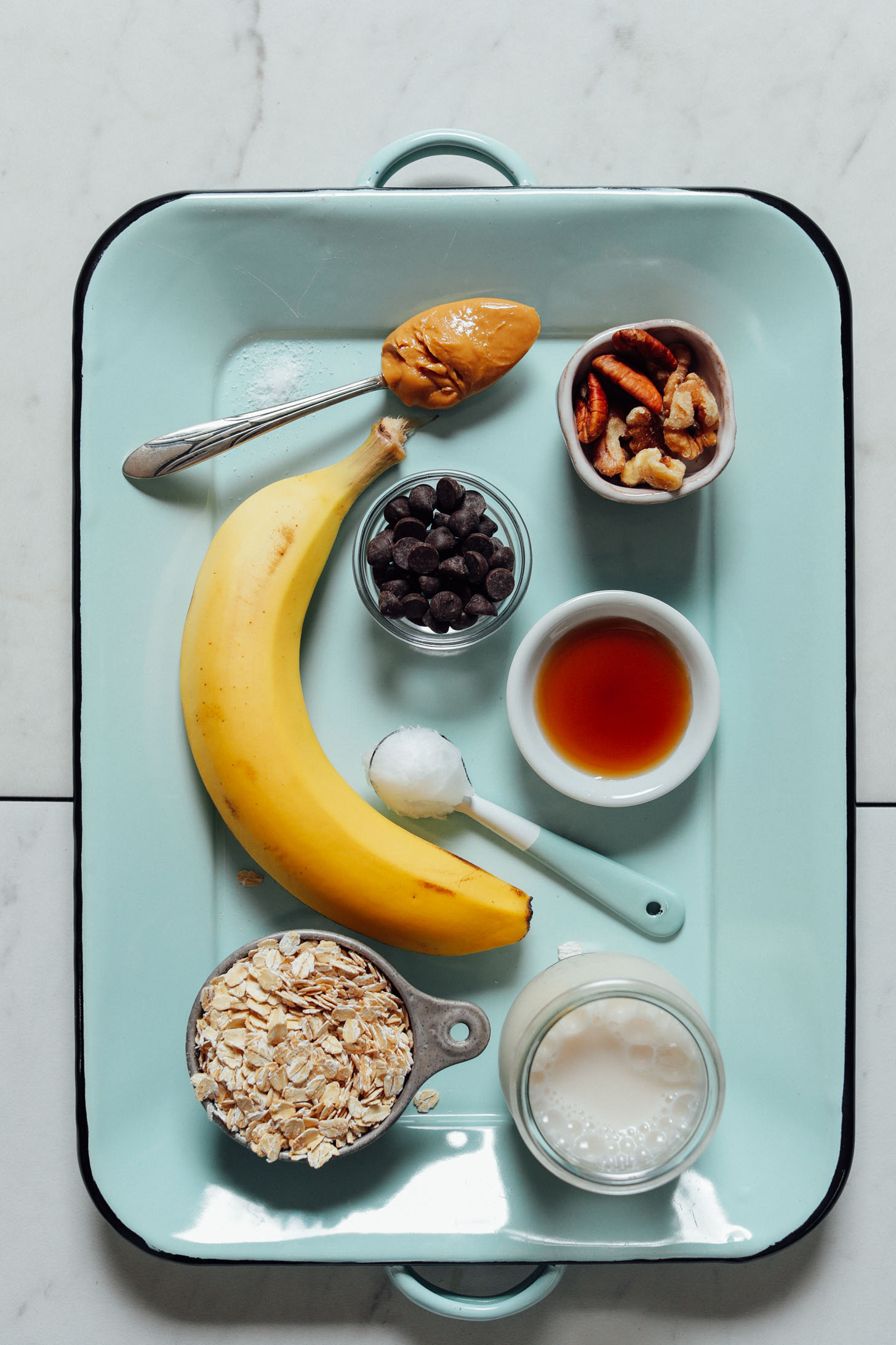 Overhead image of banana baked oatmeal ingredients on a blue tray, including oats, banana, and chocolate
