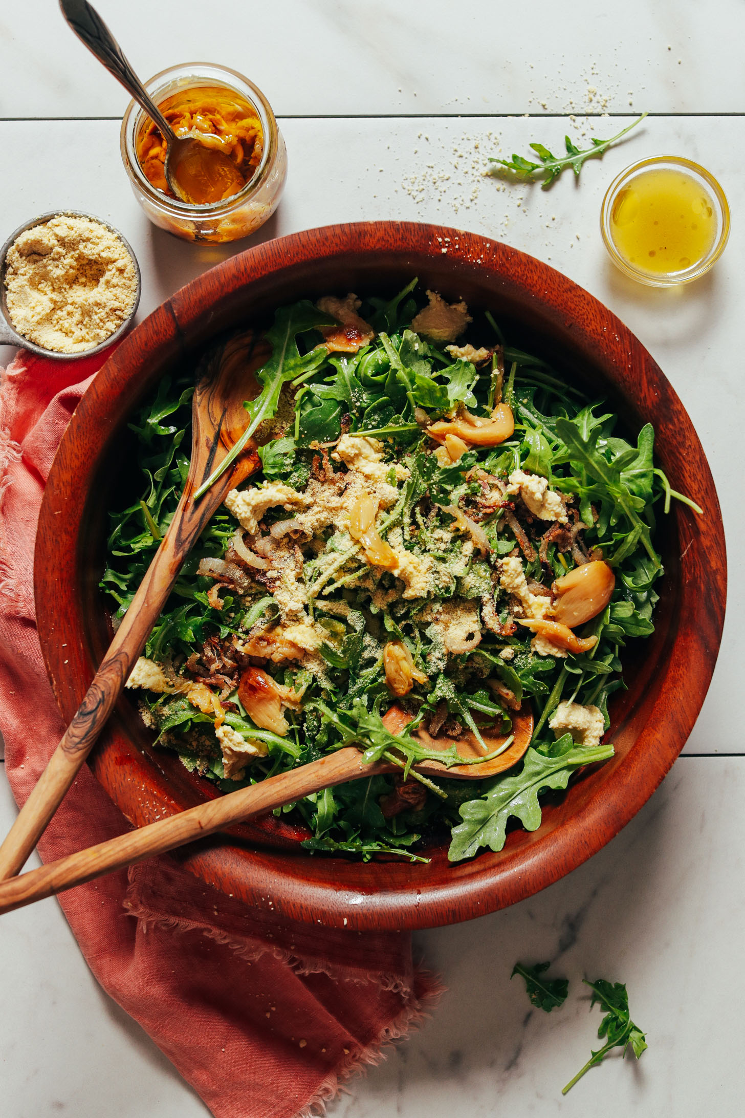 Big salad bowl filled with our Lemony Arugula Salad recipe surrounded by ingredients used to make it