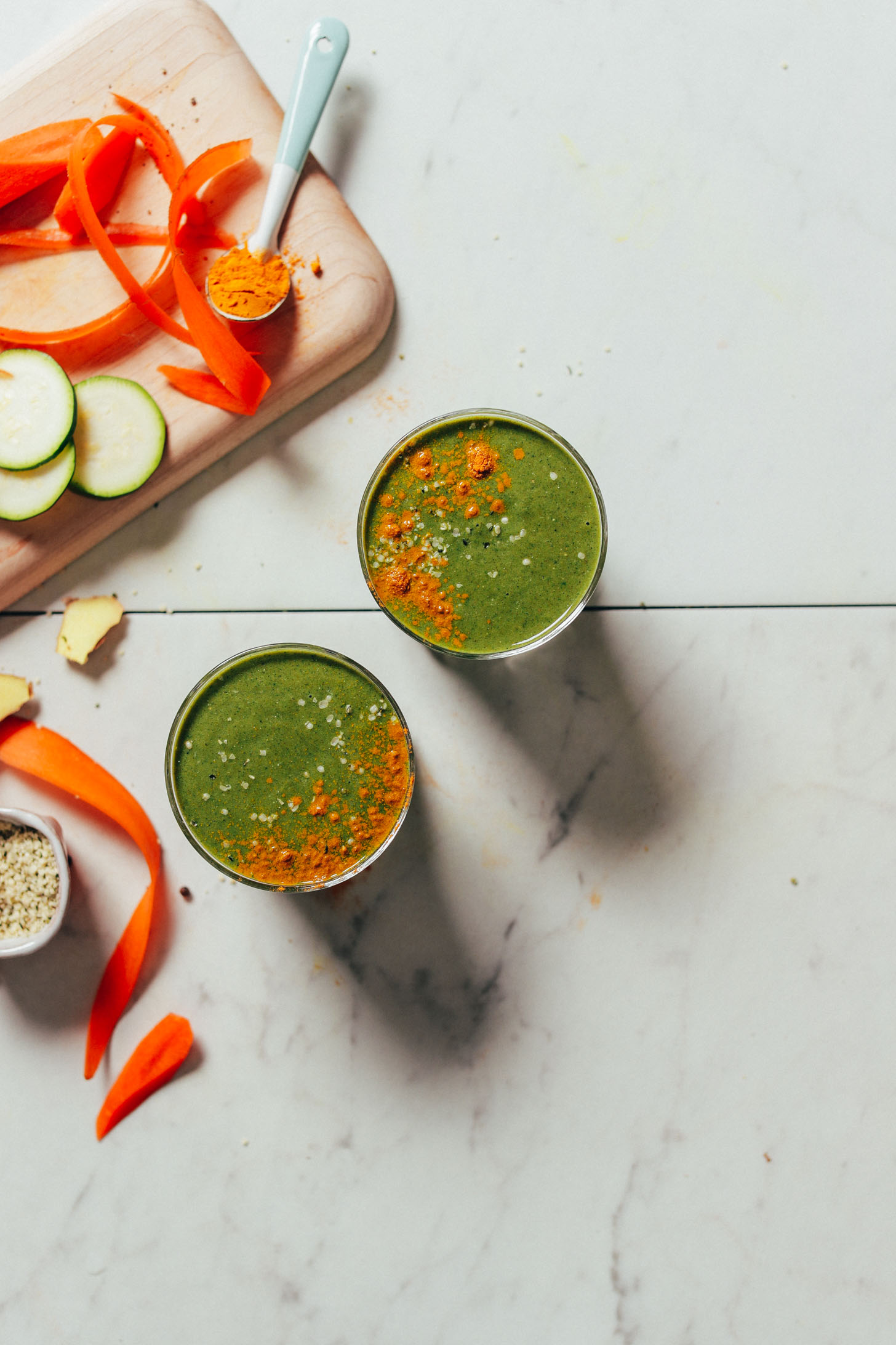 Overhead image of warming winter green smoothie garnished with hemp seeds and turmeric, and carrot, zucchini, and spoonful of turmeric on the side