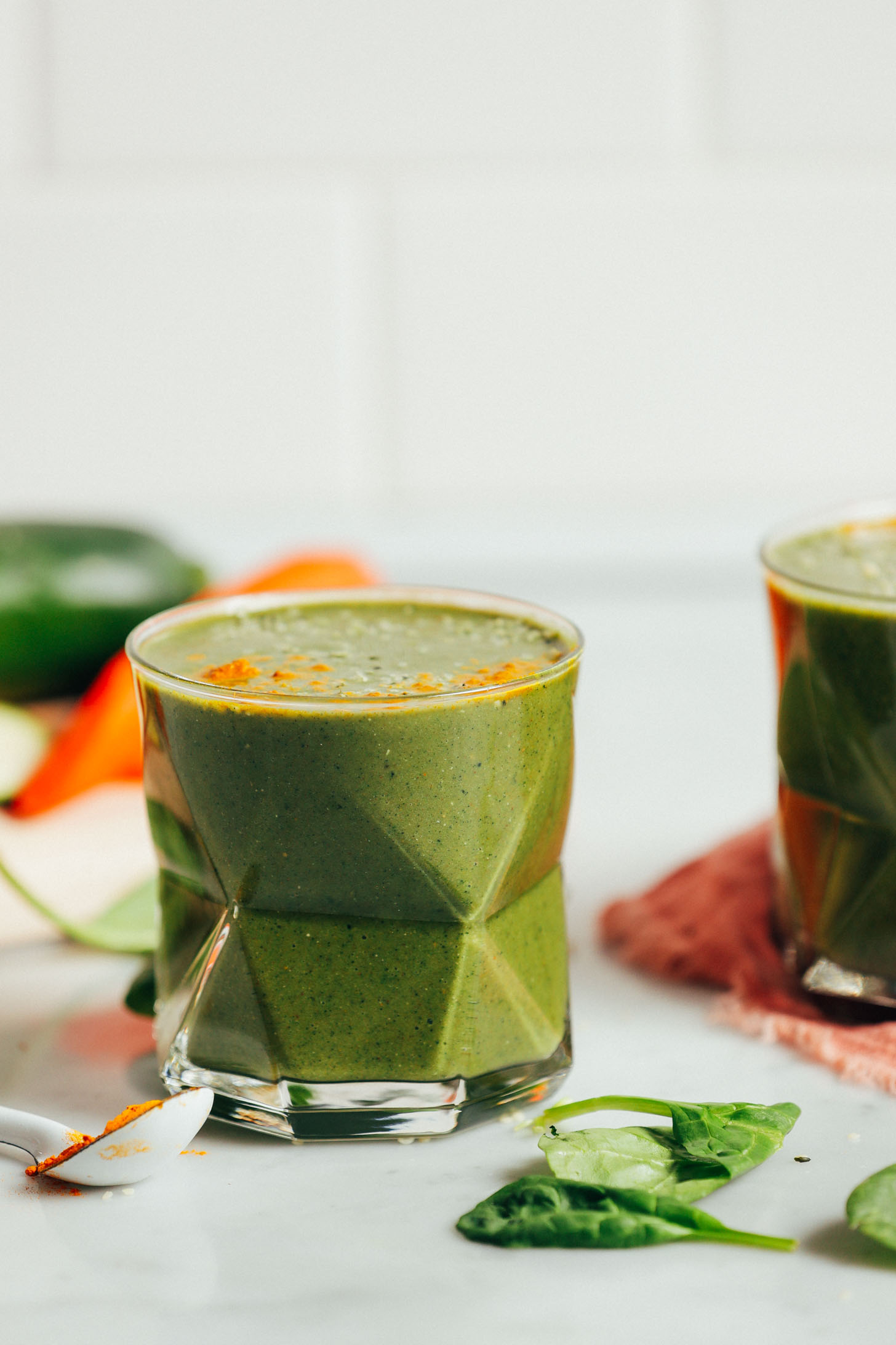 Straight on image of warming winter green smoothie in a glass with carrot, zucchini, and ground turmeric on the side