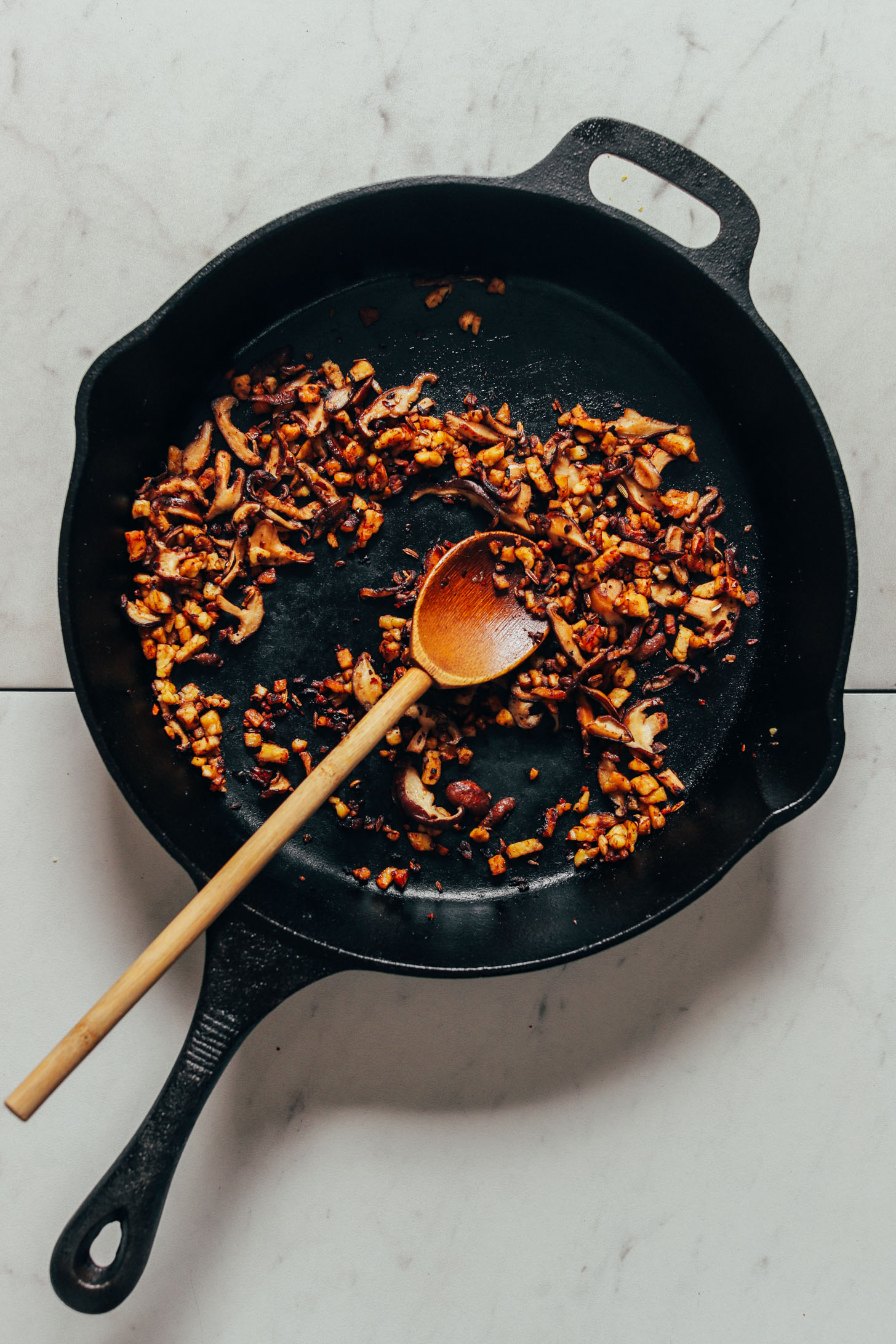 Using a wooden spoon to sauté mushrooms and tempeh in a cast-iron skillet