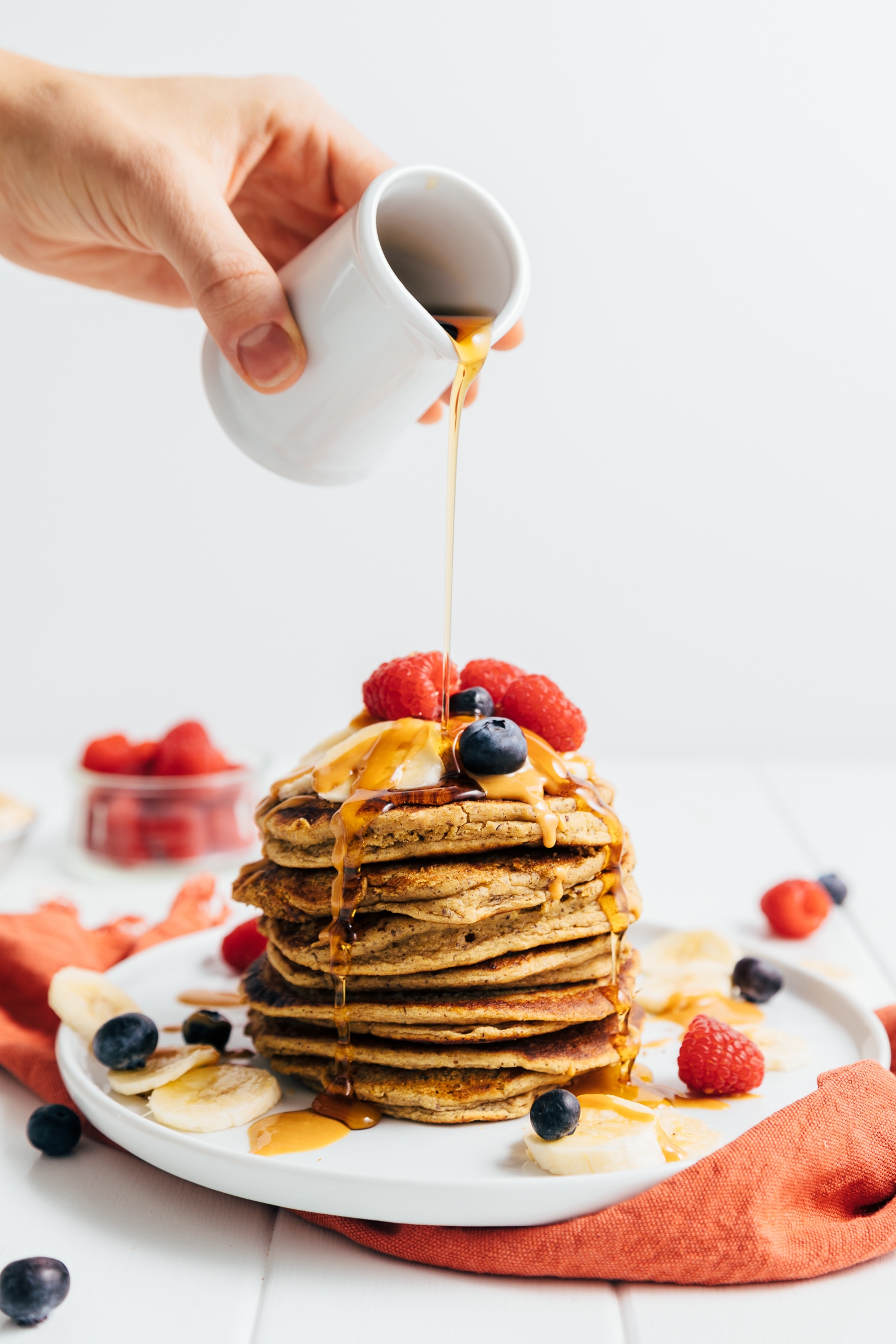 Drizzling syrup onto a stack of gluten-free Peanut Butter Protein Pancakes