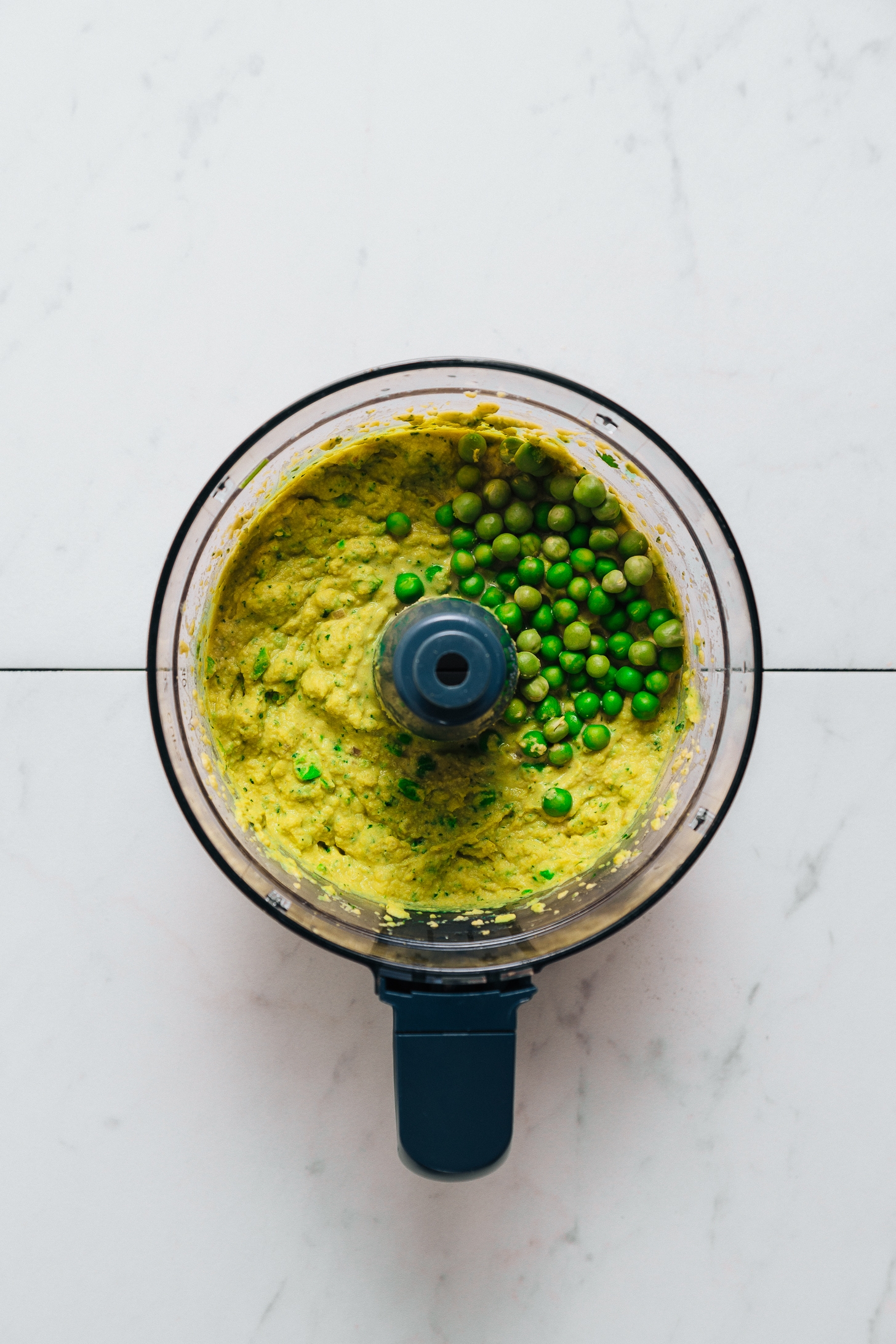 Food processor with freshly processed Green Pea Curry Hummus topped with peas