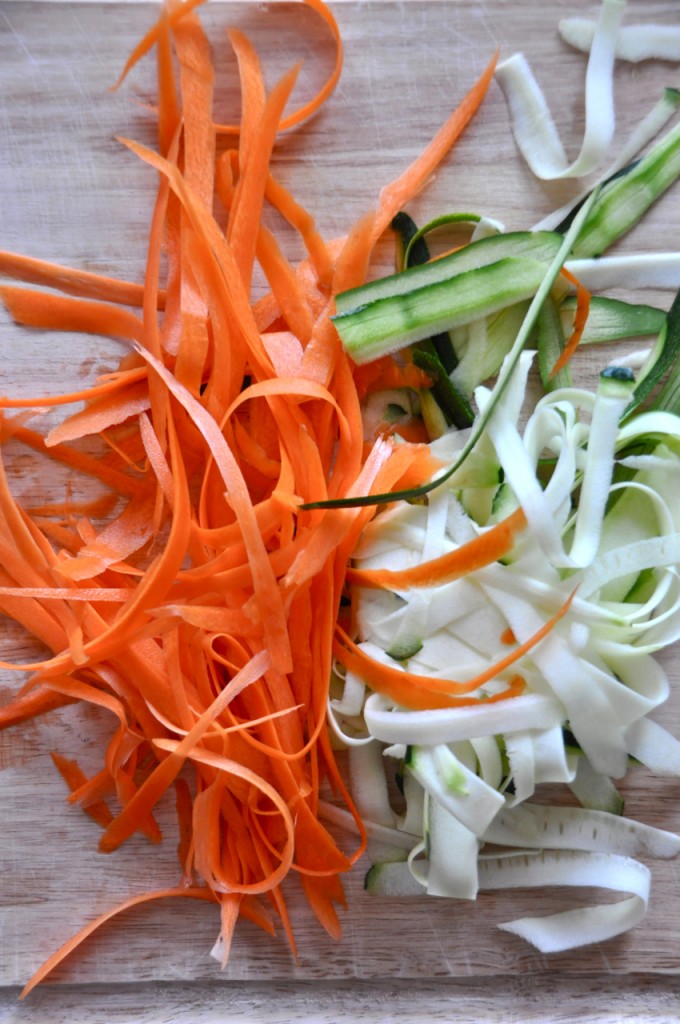 Cutting board with zucchini and carrots cut into noodle shapes with a veggie peeler