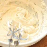 Electric mixing blades resting on a bowl filled with Honey Buttercream Frosting