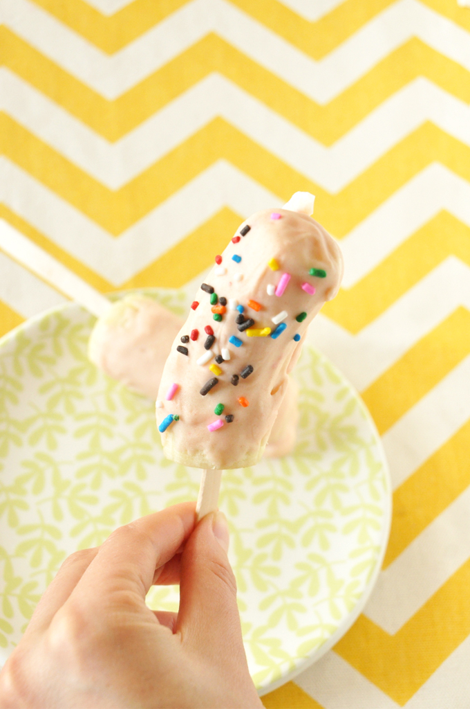 Holding up a banana pop topped with Strawberry Cake Magic Shell