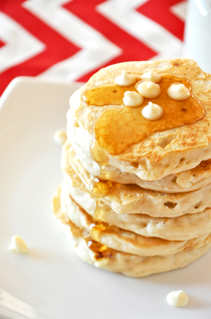 Tall stack of White Chocolate Macadamia Nut Pancakes topped with syrup and chocolate chips