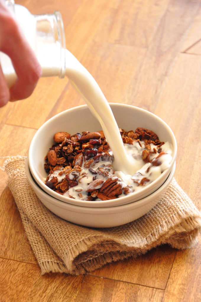 Pouring milk into a stack of bowls with the top one filled with Coconut Granola