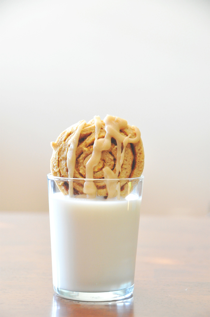 Pumpkin Cinnamon Roll Cookie resting on the rim of a glass of milk