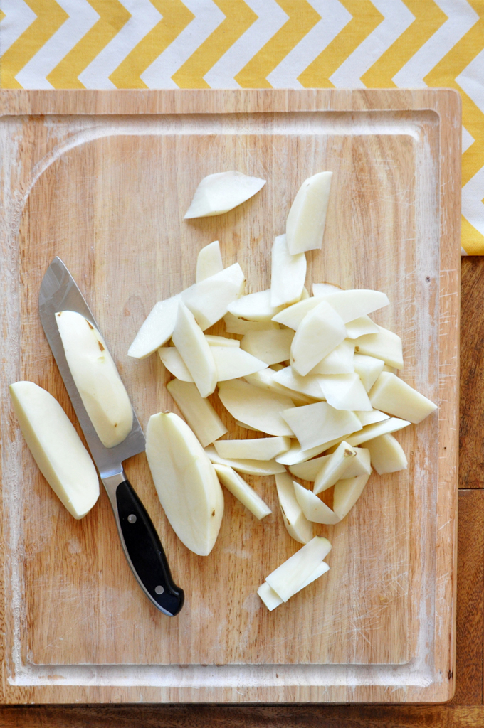 Cutting board with freshly peeled and chopped potatoes for making our Baked Rosemary Garlic Fries recipe