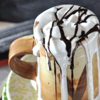 Overflowing mug of Mexican Hot Chocolate topped with Coconut Whipped Cream and chocolate sauce