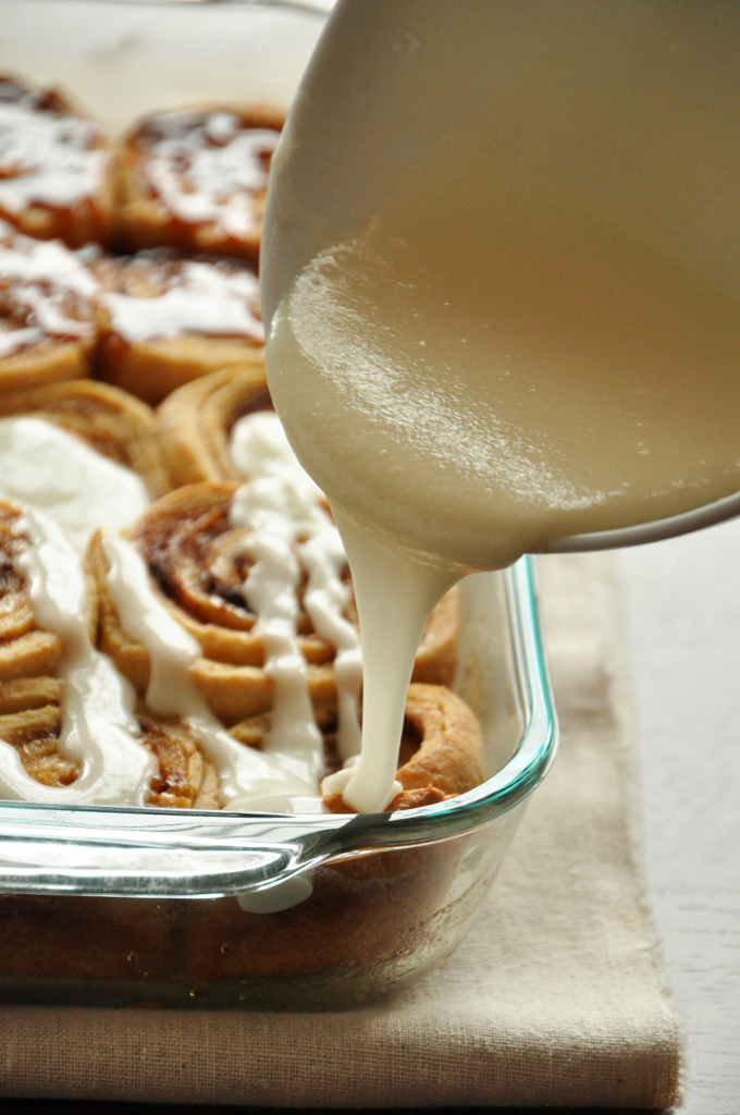 Drizzling frosting onto a batch of Overnight Honey Wheat Cinnamon Rolls for a Christmas morning treat