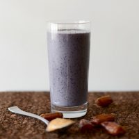 Glass of our Peanut Butter and Jelly Smoothie recipe beside dates and a spoonful of nut butter
