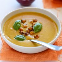 Bowl of Sweet Potato Curry Soup topped with fresh basil leaves and chickpeas
