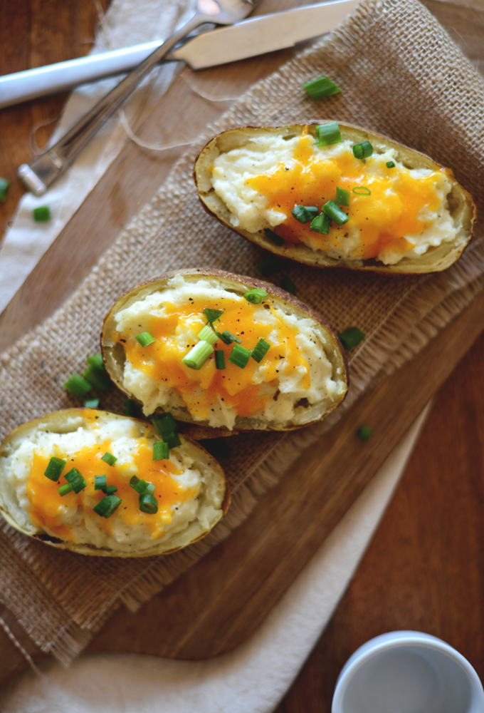 Cutting board with Cheesy Cauliflower Twice Baked Potatoes with cheddar and green onion