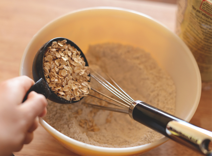 Pouring rolled oats into a bowl to make healthy Oatmeal Waffles
