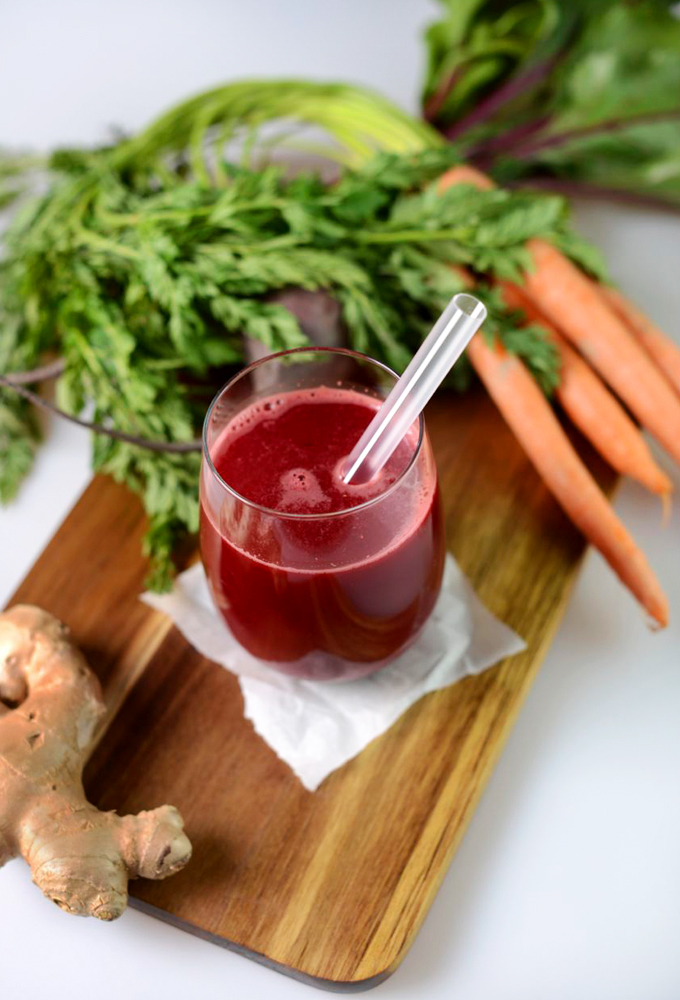 Glass of juice and cutting board with fresh carrots, beets, and ginger for making it