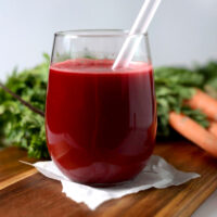 Glass of apple carrot beet ginger juice with carrots in the background