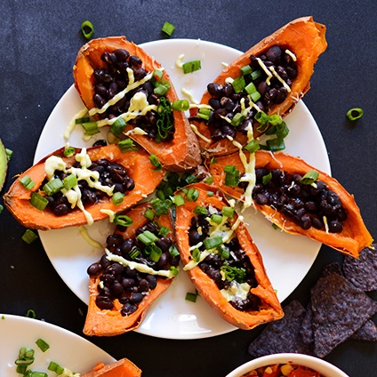 Plate of Sweet Potato Black Bean Boats topped with sliced green onion and avocado crema
