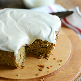 Frosted Gluten-Free Zucchini Cake on a cutting board with a slice removed