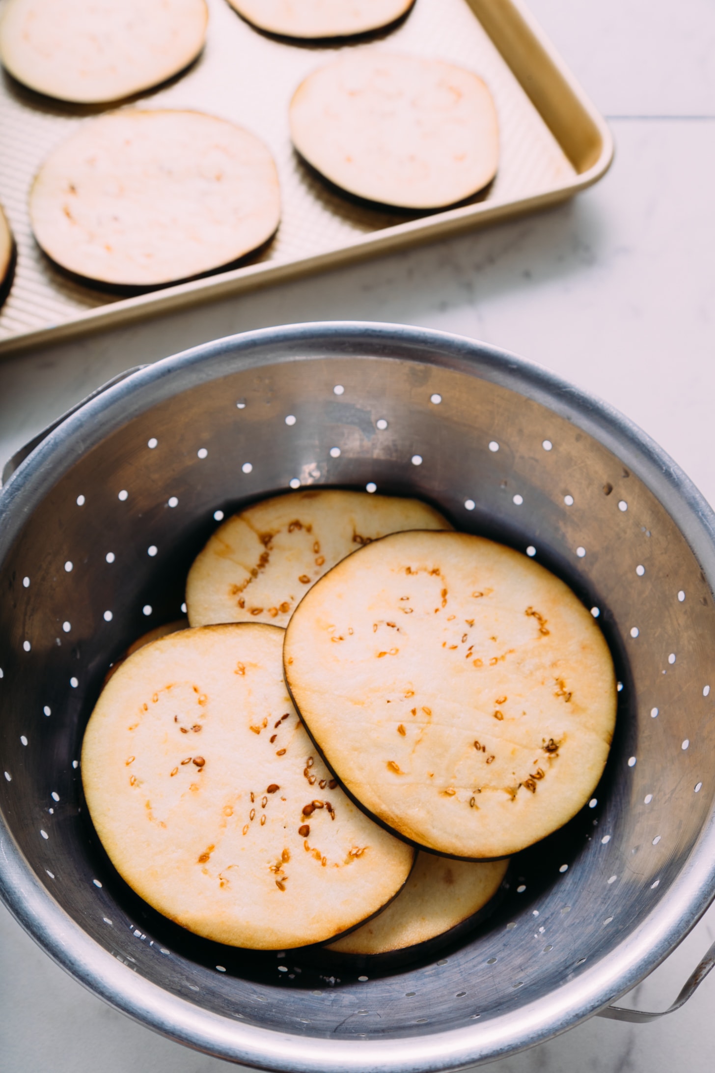 Colander and baking sheet of eggplant rounds