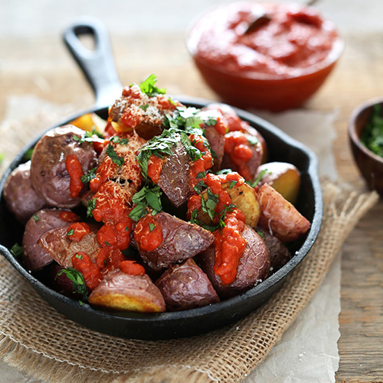 Cast-iron skillet piled high with Patatas Bravas topped with Spicy Sauce