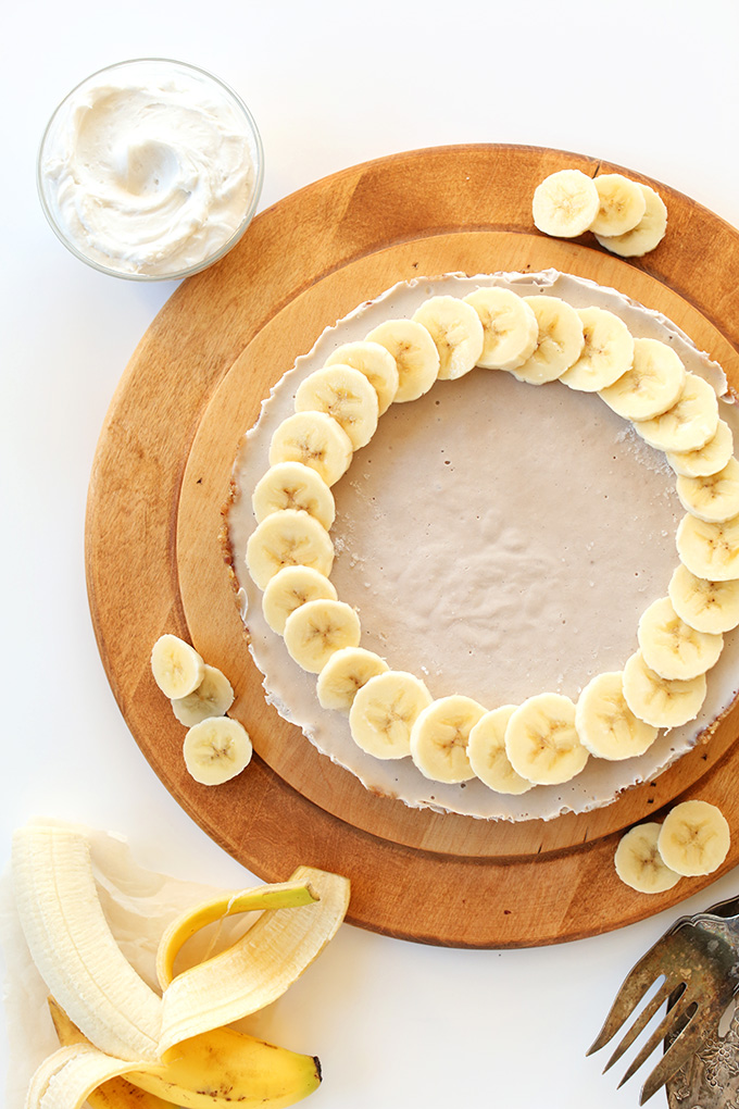 Raw Vegan Banana Cream Pie on a cutting board with a bowl of coconut cream