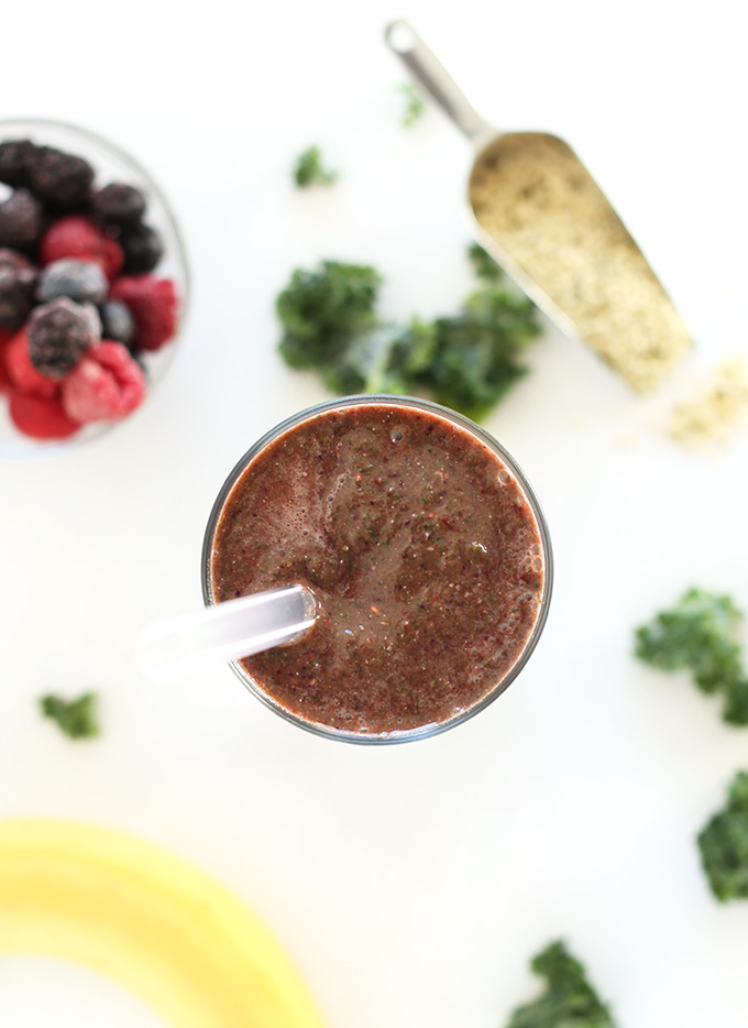 Glass of our Hide Your Kale Pomegranate Smoothie surrounded by ingredients used to make it