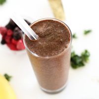 Tall glass of our Hide Your Kale Pomegranate Smoothie recipe beside fresh berries and kale