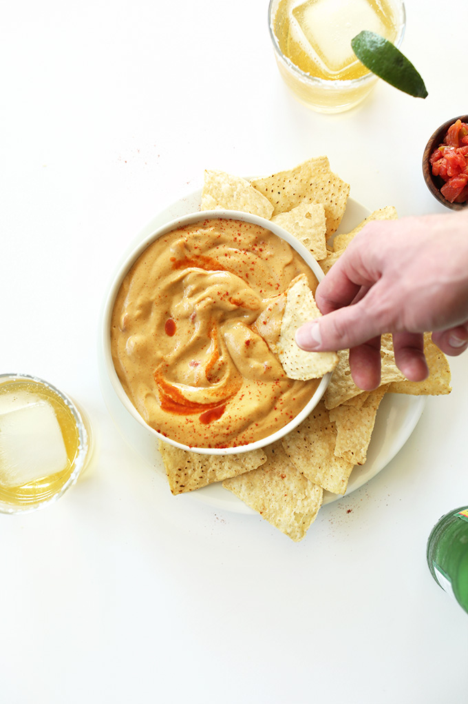 Dipping a tortilla chip into a bowl of Cashew-Free Vegan Queso Dip