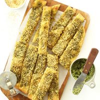 Batch of homemade Vegan Pesto Breadsticks on a parchment-lined cutting board