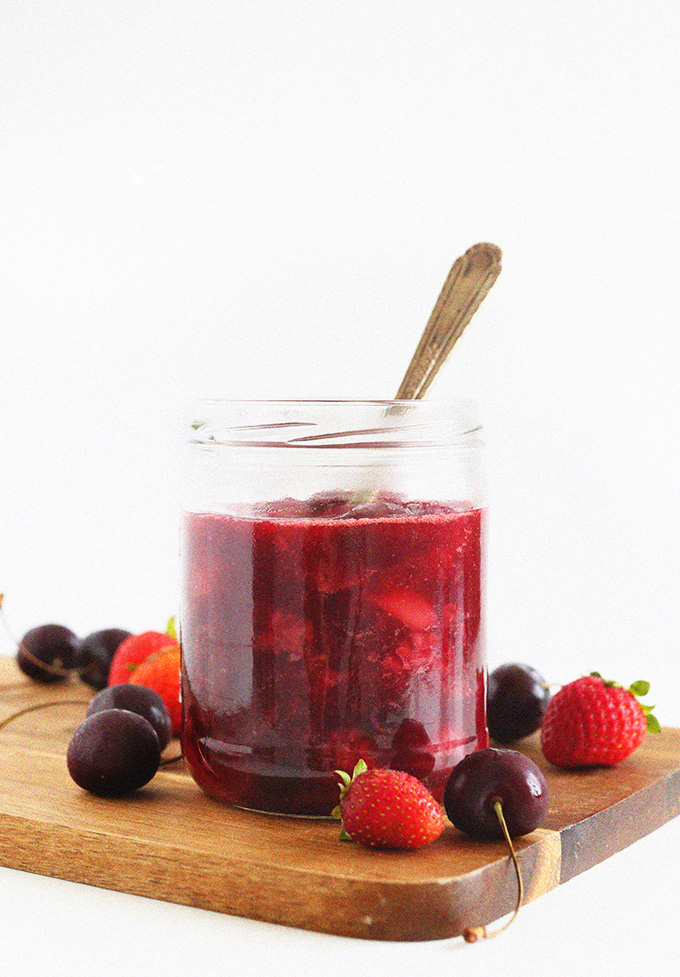 Jar of homemade fruit compote surrounded by fresh strawberries and cherries