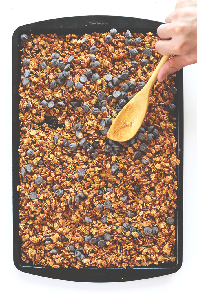 Using a wooden spoon to mix a tray of Peanut Butter Chocolate Chip Granola