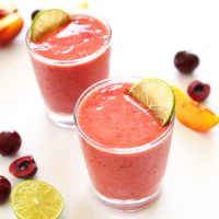 Two glasses of our Cherry Limeade Smoothie recipe beside fruit used to make it