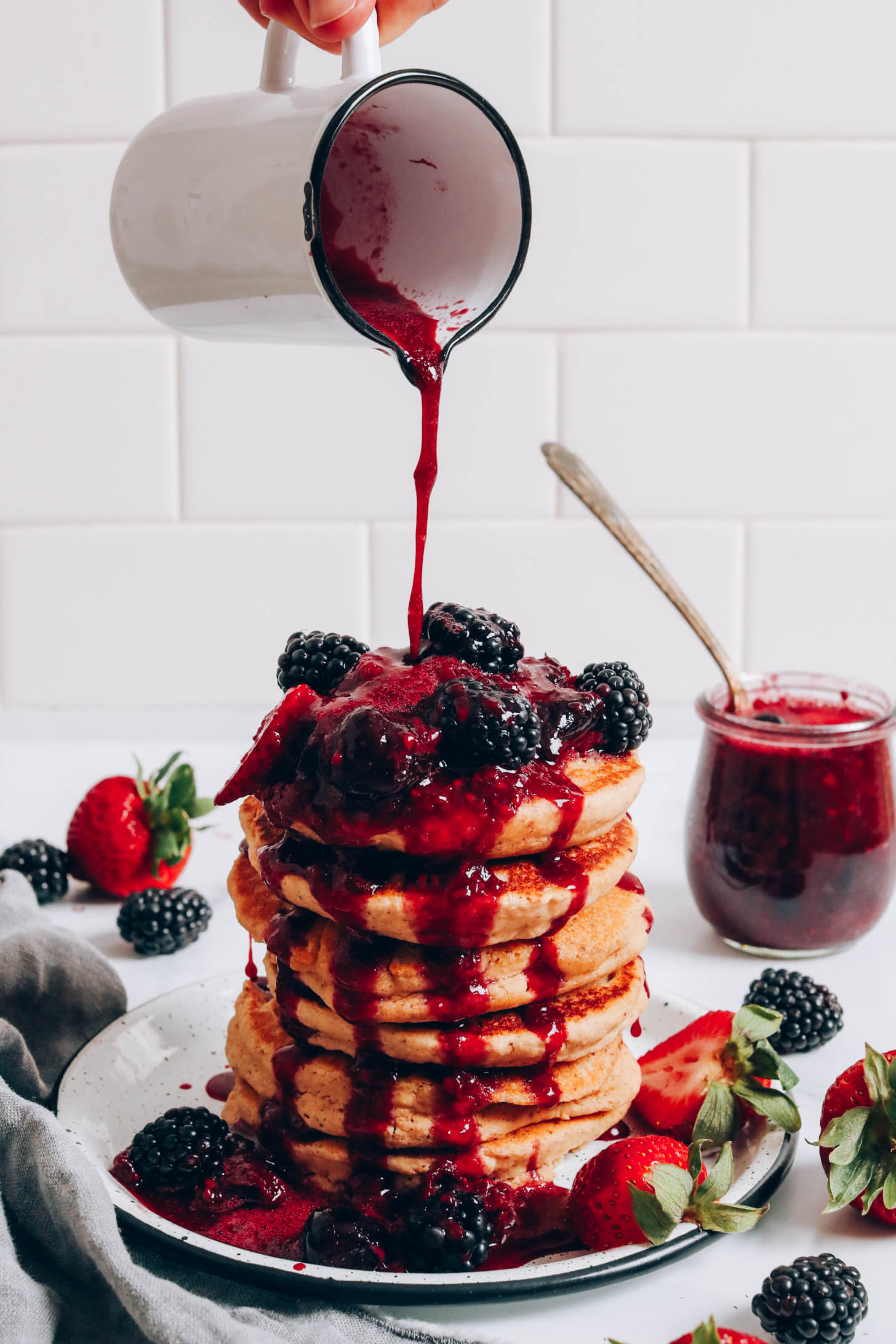 Pouring mixed berry compote onto a stack of gluten-free pancakes