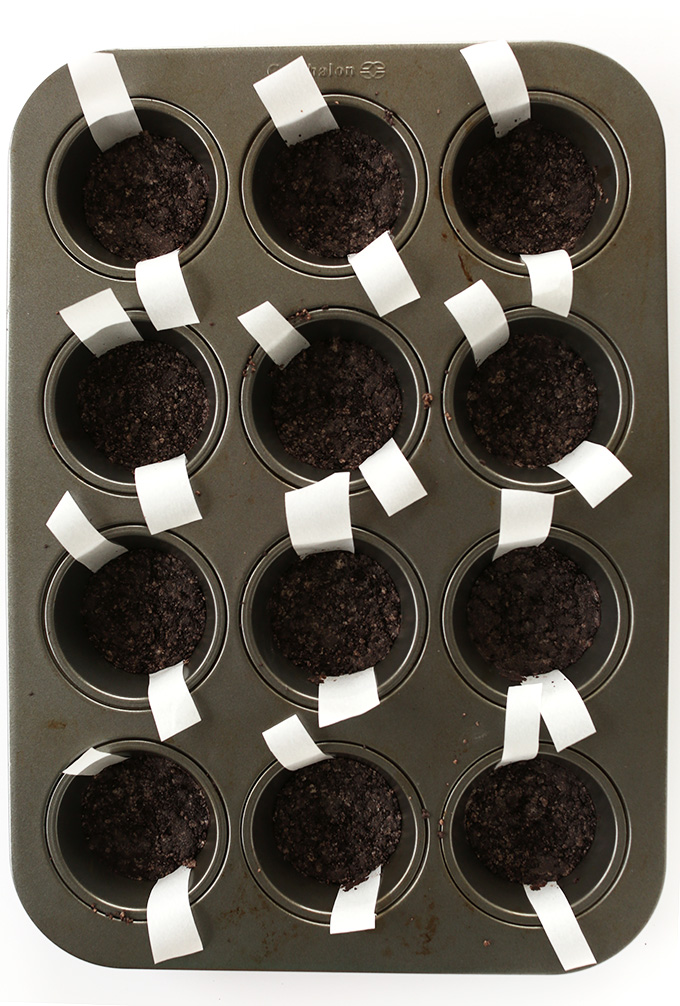 Muffin tin with oreo cookie crusts and parchment paper tabs for easy removal