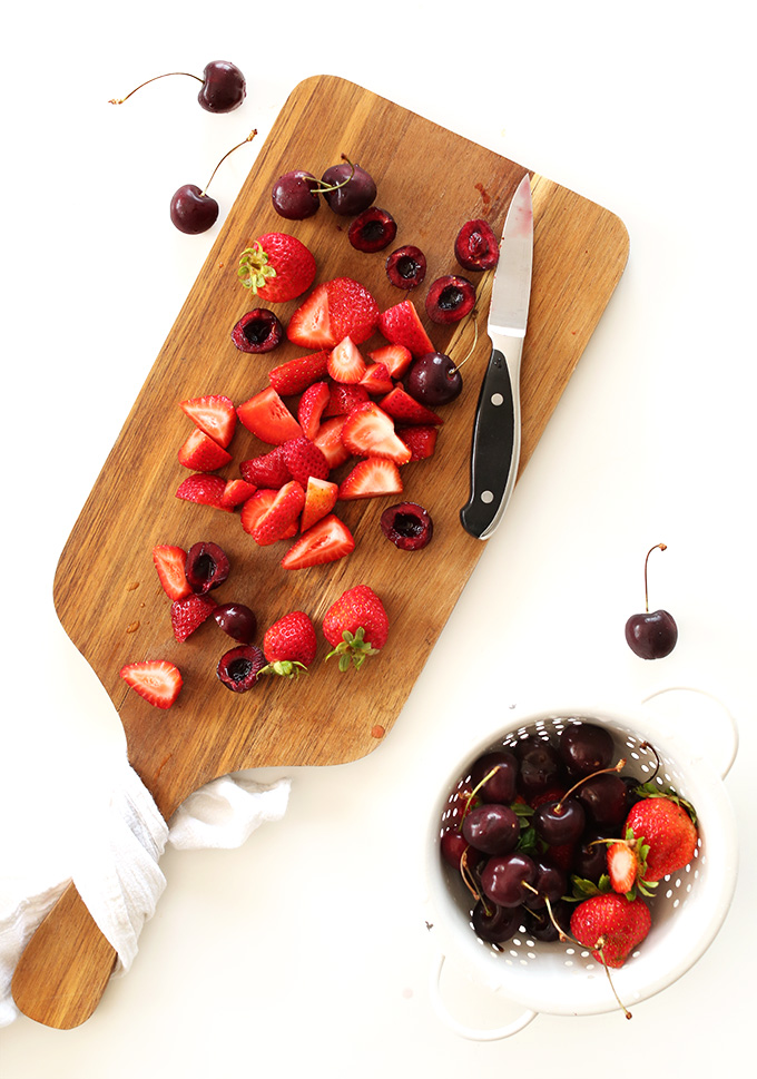 Cutting board and colander filled with sliced strawberries and cherries for making fruit compote