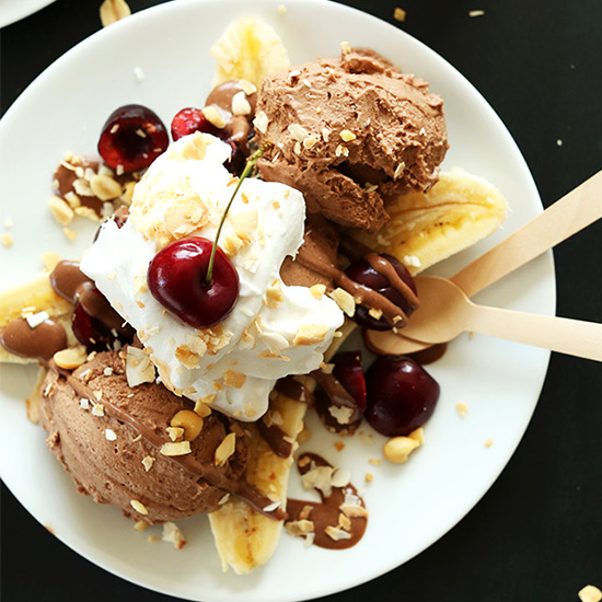 Plate filled with a Vegan Banana Split made with chocolate ice cream, peanuts, cherries, and coconut whip
