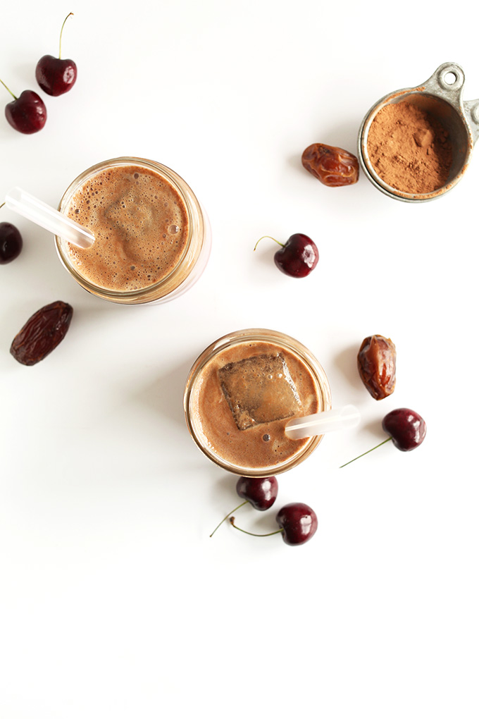 Glasses of Chocolate Cherry Almond Milk surrounded by ingredients used to make the recipe